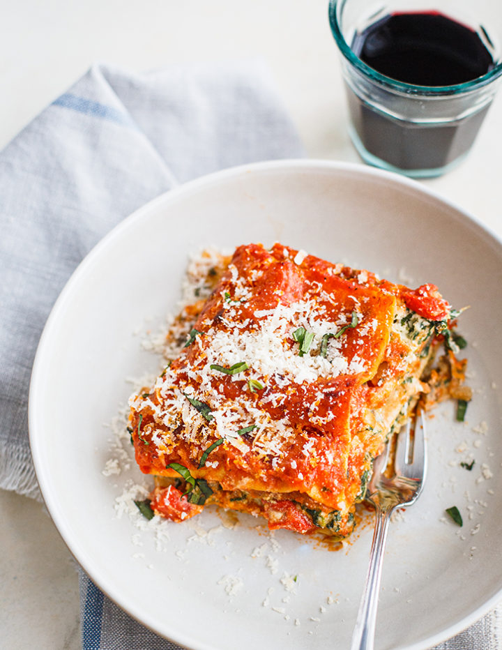 slice of lasagna on a white plate with a glass of red wine