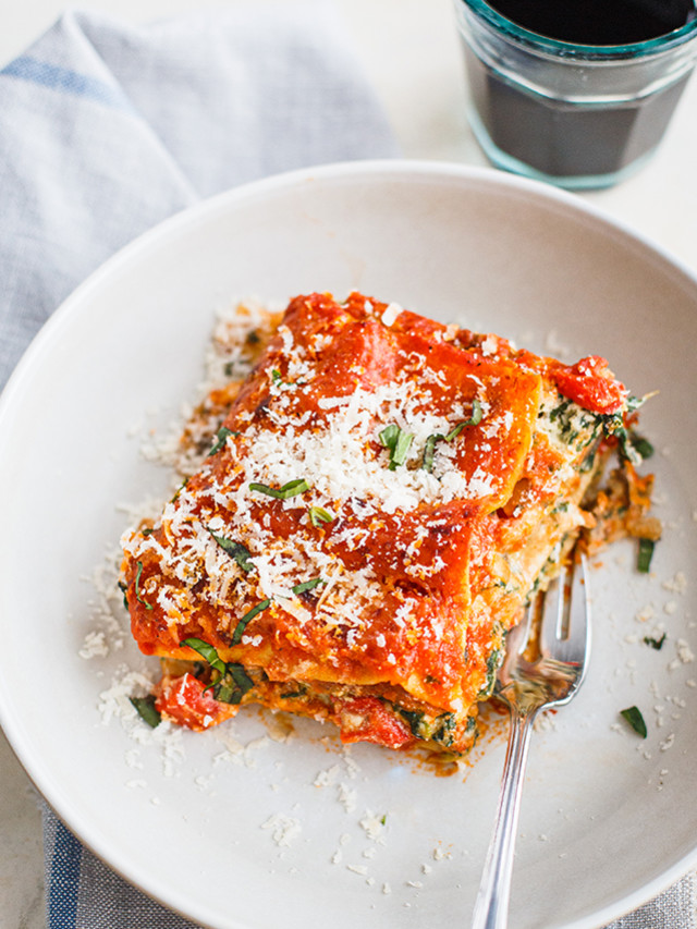 slice of lasagna on a white plate with a glass of red wine