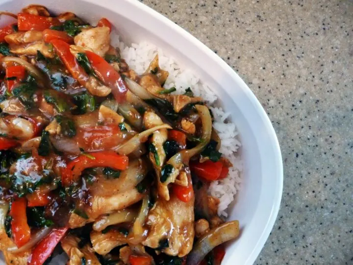 Chicken and pepper stir fry over rice on a white plate.