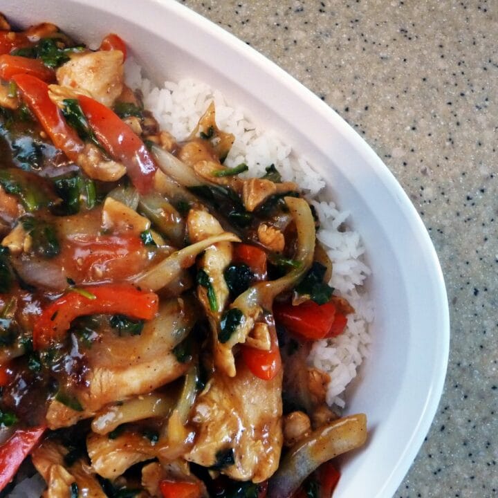 Chicken and pepper stir fry over rice on a white plate.