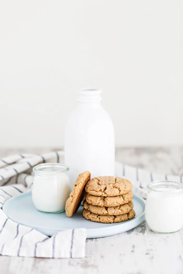a stack of almond butter cookies next to a glass of milk