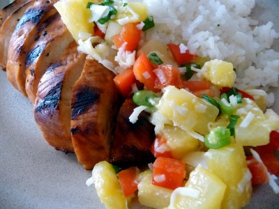 A plate of sliced pineapple salsa chicken with coconut rice on the side.