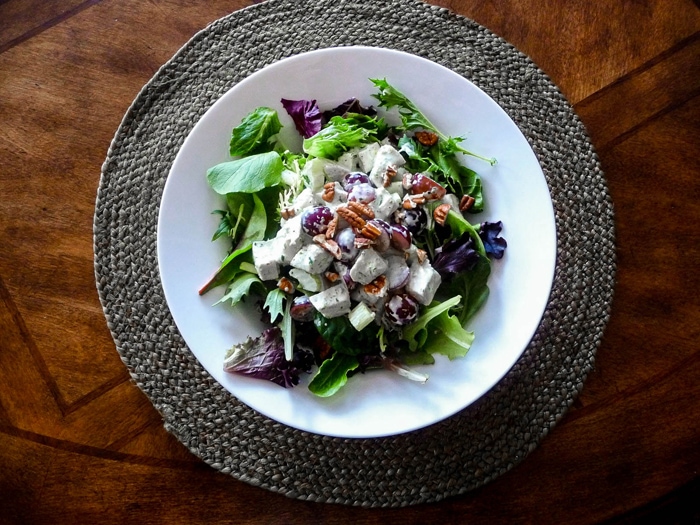 tarragon chicken salad served on a bed of greens on a white plate