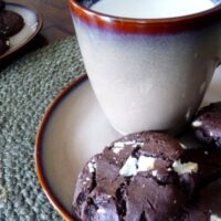 Triple chocolate chunk cookies on a small plate with a mug of milk.