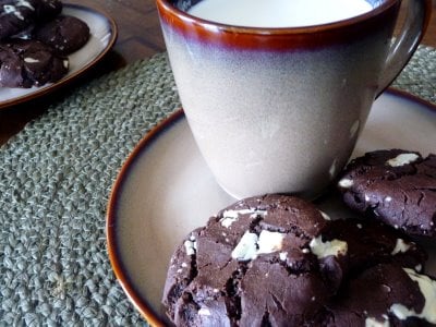 Triple chocolate chunk cookies on a small plate with a mug of milk.