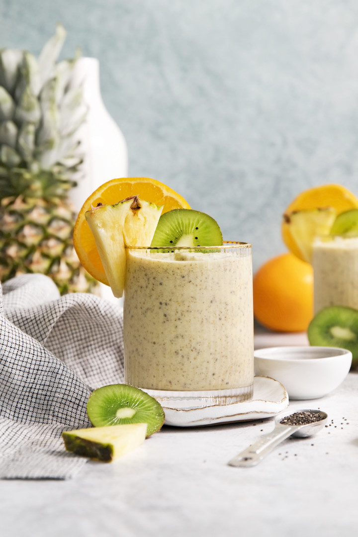 glass filled with a pineapple orange smoothie garnished with fresh orange, pineapple, and kiwi