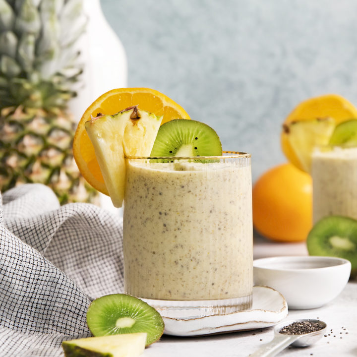 glass filled with a pineapple orange smoothie garnished with fresh orange, pineapple, and kiwi