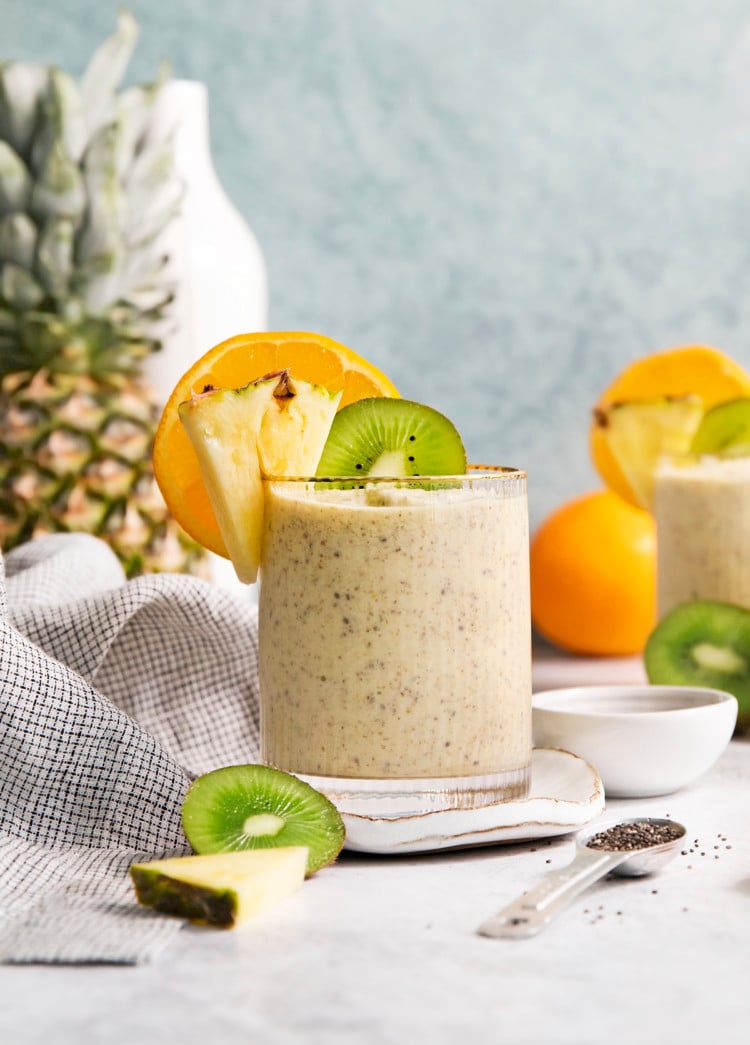 glass filled with a pineapple orange smoothie garnished with fresh orange, pineapple, and kiwi