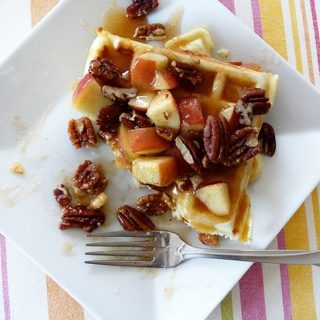 waffles on a white plate with syrup, apples, and pecans