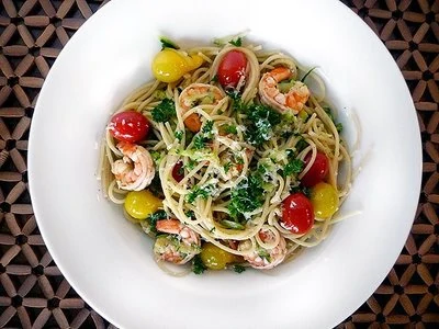 overhead view of a white bowl of shrimp scampi with tomatoes.