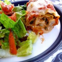 A spinach lasagna roll on a plate with a side salad.