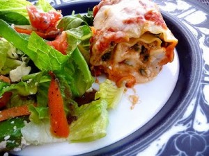 A spinach lasagna roll on a plate with a side salad.