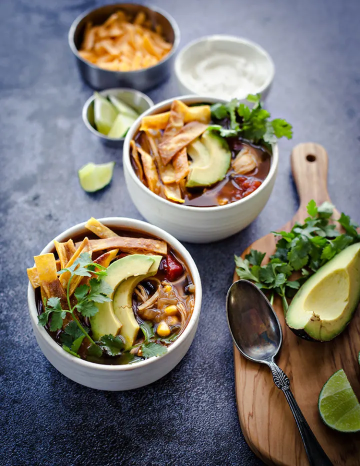 white bowls of chicken tortilla soup with garnishes on a kitchen counter