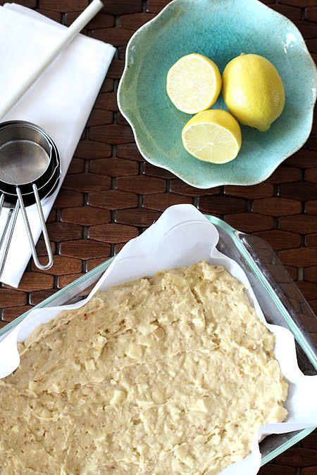 Overhead view of a pan of coconut white chocolate blondie batter next to a bowl of lemons. 