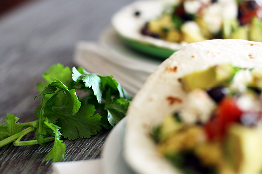 close up of fresh cilantro next to a plate of black bean breakfast burritos