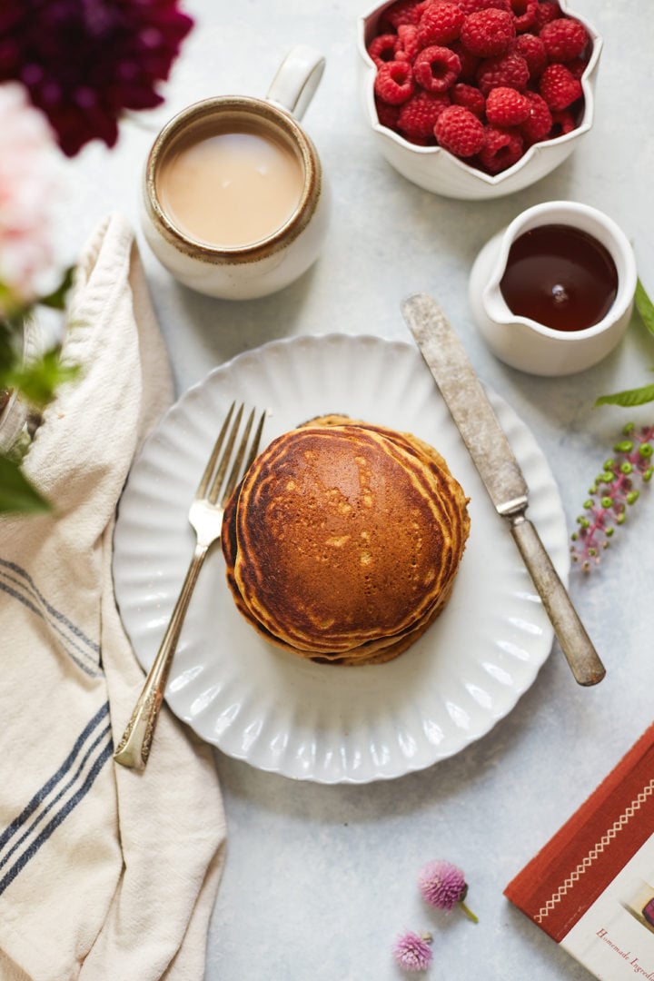 overhead photo of a table set with a plate of the best multigrain pancakes, coffee, and fresh raspberries