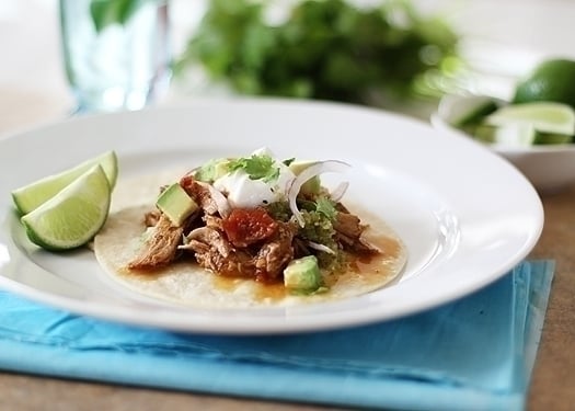 A white plate with a shredded pork tacos and lime wedges on it.