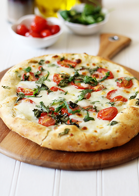 A pizza caprese with focaccia crust on a wooden pizza peel.