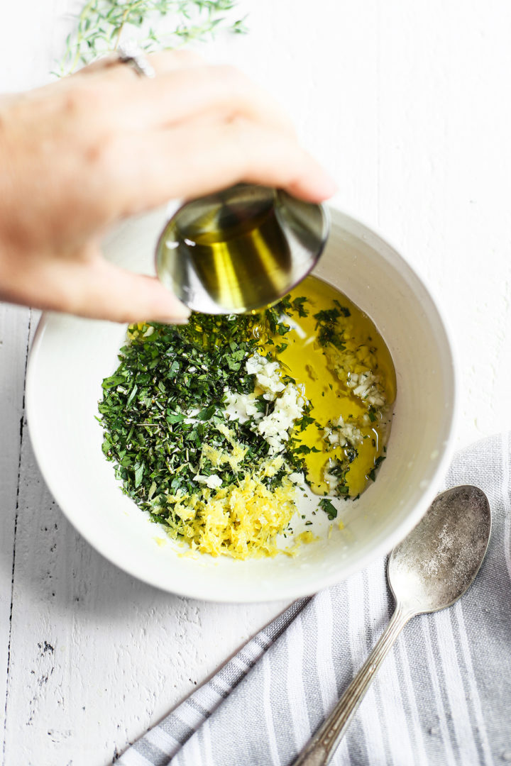 woman adding olive oil to a bowl of gremolata ingredients