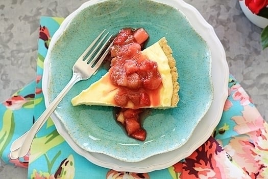 Overhead view of a slice of lemon curd tart topped with strawberry rhubarb compote on a blue plate. 