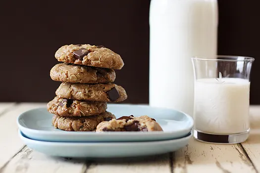 almondcookies A stack of chocolate chip almond butter oatmeal cookies on a blue plate, next to a jug and glass of milk.