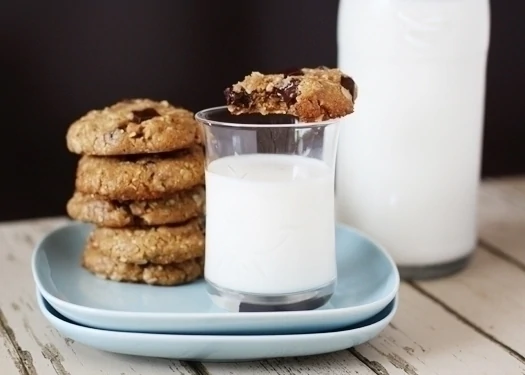 almondoatmealchewycookies2 Oatmeal almond butter chocolate chip cookies on a blue plate with a glass of milk. One cookie rests on the rim of the glass.