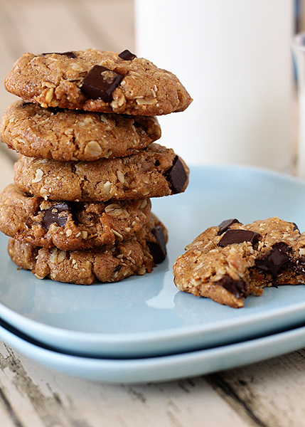A stack of chocolate chip almond butter oatmeal cookies on a blue plate, next to a jug and glass of milk. 