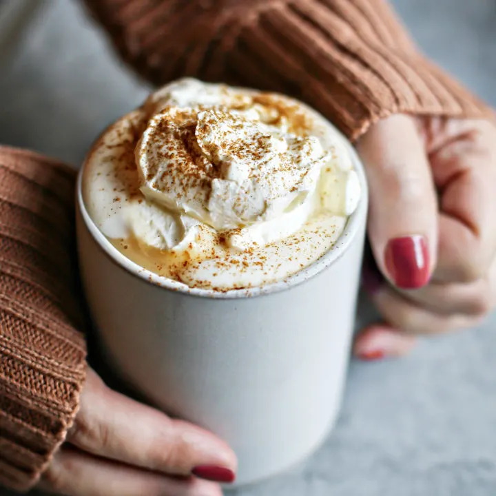 photo of woman holding a mug of pumpkin hot chocolate with vanilla whipped cream