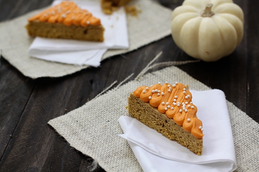 Pumpkin cookie bars topped with frosting on white napkins. 