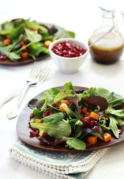 two brown plates of roasted butternut squash salad, with dressing and pomegranate arils on the side. 