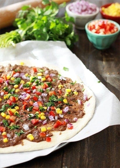 A homemade mexican pizza topped with black bean spread and veggies. 