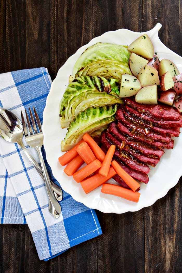 sliced baked corned beef with mustard and brown sugar on plate with potatoes, carrots, and cabbage