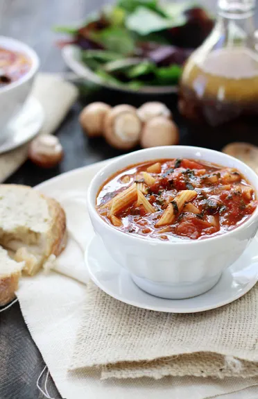 A bowl of tomato florentine soup, with a bottle of dressing and a green side salad in the background. 