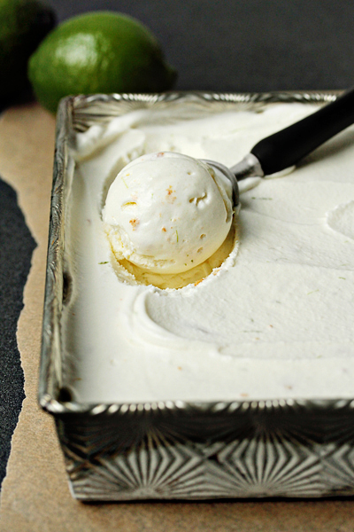 Key lime pie ice cream in a metal container, being scooped out. 