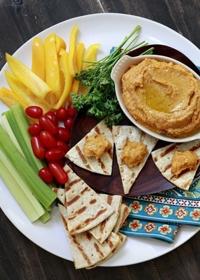 overhead photo roasted red pepper hummus on a serving platter with pita bread and raw vegetables