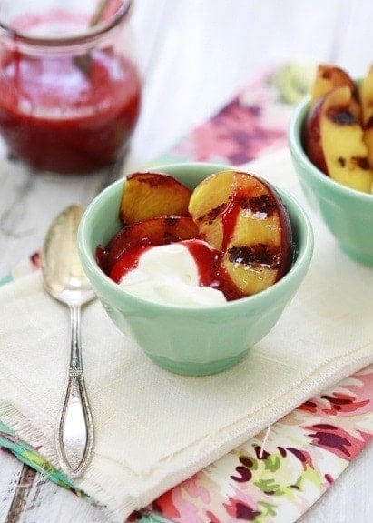 a photo of a recipe for grilled peaches with mascarpone and raspberry in a small green bowl with a spoon