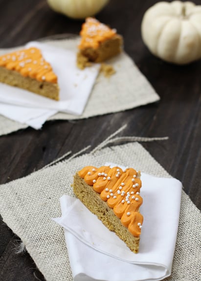 Pumpkin cookie bars topped with frosting on white napkins. 