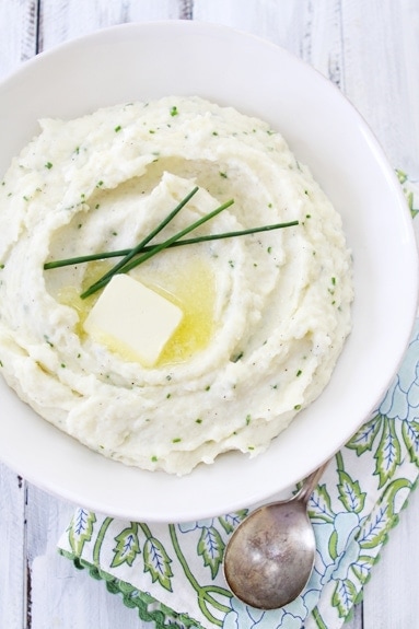 Overhead view of mascarpone mashed potatoes in a white serving bowl, garnished with chives. 