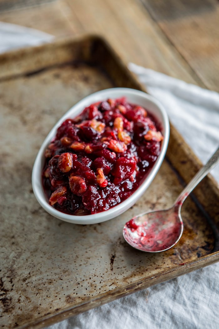 cranberry orange relish in white serving dish on baking tray next to spoon