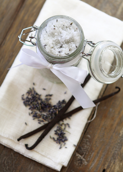 Overhead view of a jar of homemade sugar scrub, next to vanilla beans and dried lavender. 
