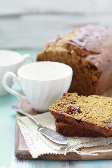 photo of slices of cranberry pumpkin bread on a wooden cutting board next to a loaf of pumpkin bread