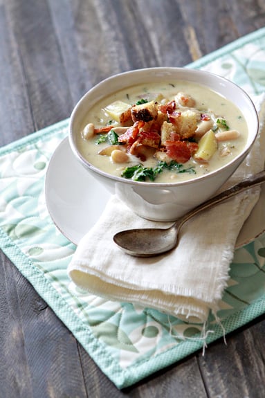 a white bowl of rosemary chicken chowder with white beans topped with homemade croutons and crumbled bacon