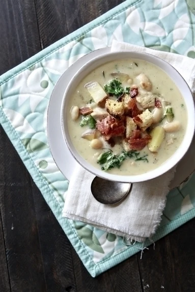 A bowl of cheesy chicken potato chowder with a spoon and napkin. 