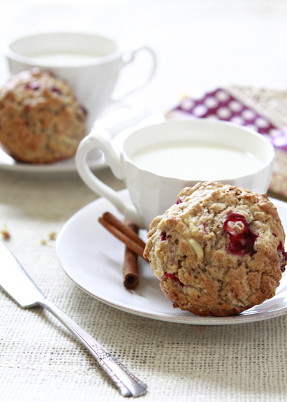 An apple cranberry muffin from this cranberry muffins recipe on a white saucer with a cup of tea. 