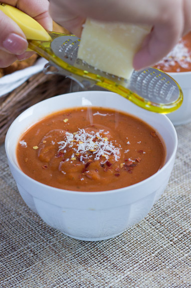 Parmesan cheese being grated over a bowl of fire roasted tomato bisque. 