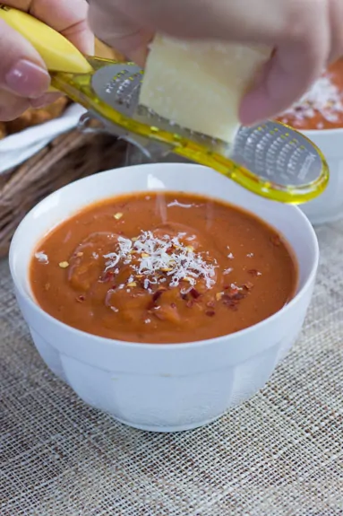 Parmesan cheese being grated over a bowl of fire roasted tomato bisque.