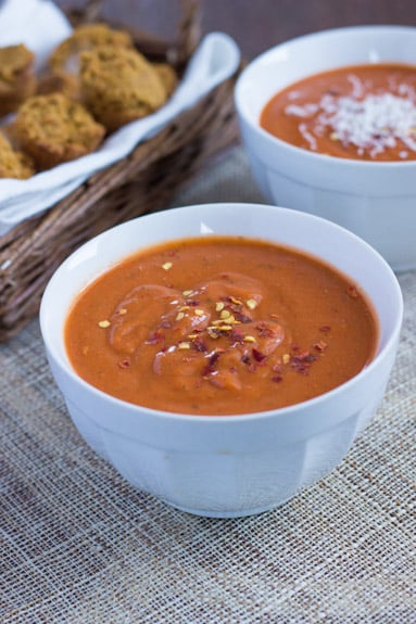 Two bowls of vegan tomato bisque, with a basket of rolls in the background. 