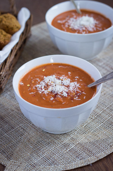 Two bowls of vegan tomato bisque, with a basket of rolls in the background. 