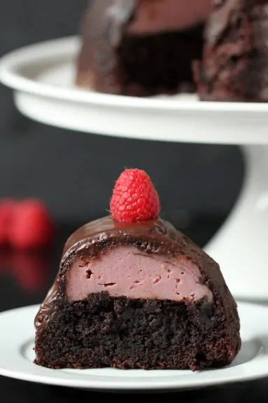 A slice of chocolate cake with raspberry filling on a plate. The rest of the bundt cake rests in the background. 