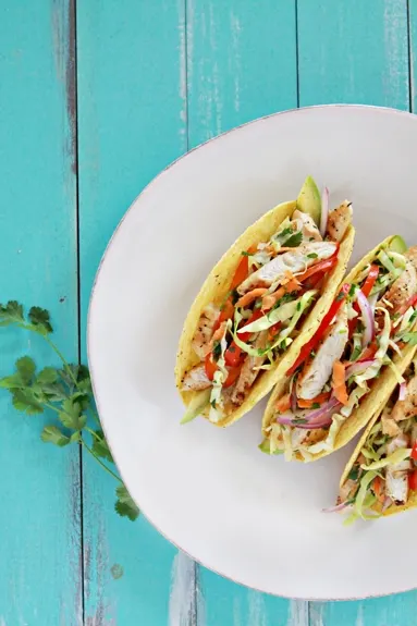 overhead shot of a photo of Easy Lemon Pepper Chicken Tacos with Slaw on a bamboo tray with an aqua background